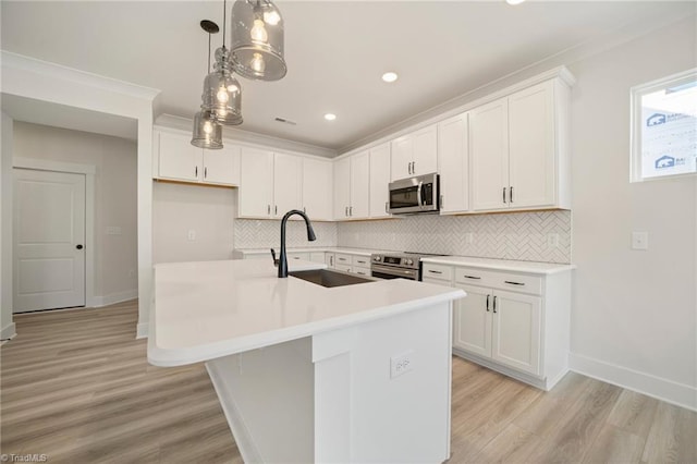 kitchen featuring decorative light fixtures, sink, white cabinetry, appliances with stainless steel finishes, and an island with sink