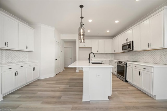 kitchen featuring pendant lighting, white cabinets, stainless steel appliances, sink, and a kitchen island with sink