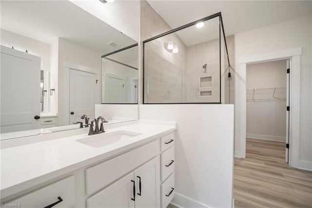 bathroom with wood-type flooring, tiled shower, and vanity