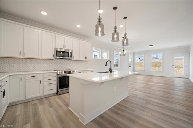 kitchen featuring pendant lighting, white cabinets, stainless steel appliances, an island with sink, and sink