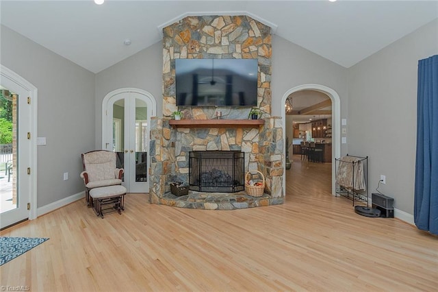 living room featuring a stone fireplace, high vaulted ceiling, and light hardwood / wood-style flooring