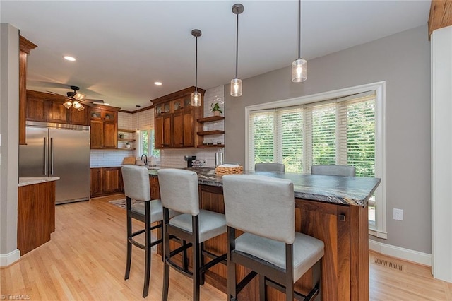 kitchen featuring decorative backsplash, built in fridge, hanging light fixtures, and light hardwood / wood-style flooring