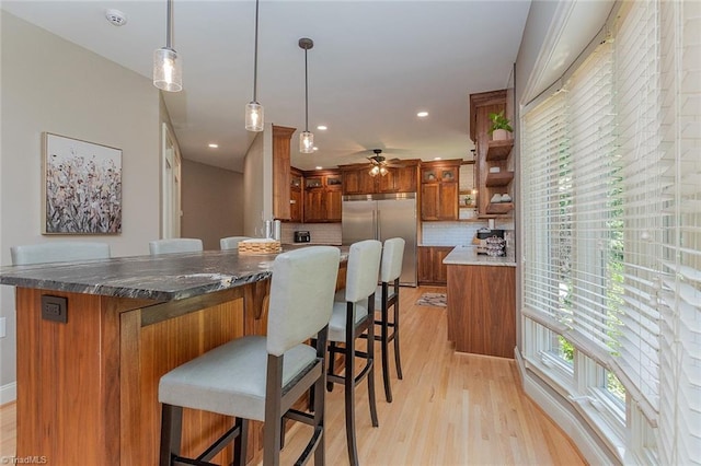 kitchen with a breakfast bar area, hanging light fixtures, stainless steel built in refrigerator, decorative backsplash, and light wood-type flooring