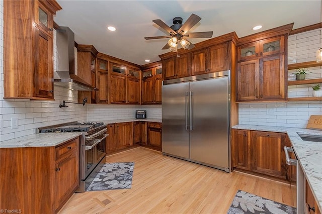 kitchen featuring high end appliances, light hardwood / wood-style flooring, light stone countertops, and wall chimney exhaust hood