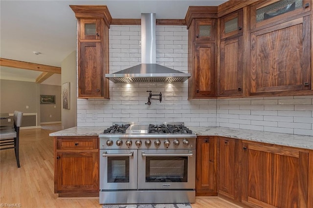 kitchen featuring light stone counters, decorative backsplash, wall chimney exhaust hood, and range with two ovens