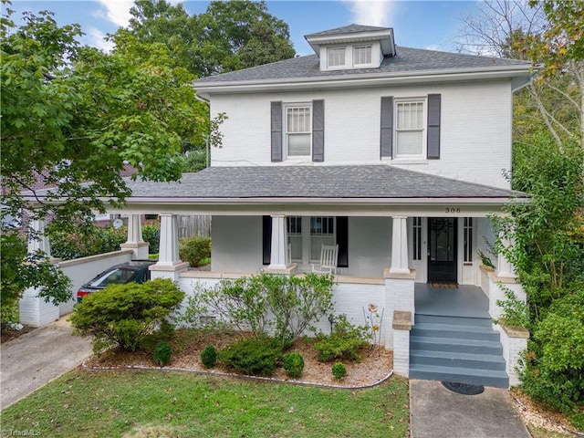 american foursquare style home with covered porch, roof with shingles, and brick siding