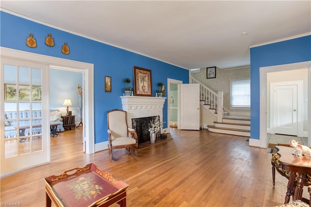 living room with a brick fireplace, baseboards, stairway, and wood finished floors