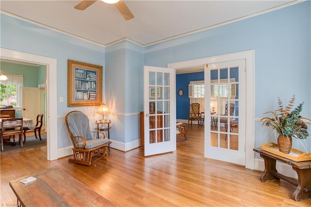 living area featuring french doors, light wood-style floors, ornamental molding, ceiling fan, and baseboards