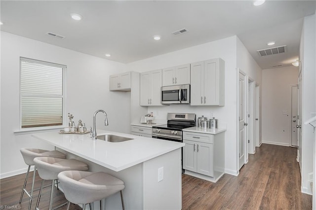 kitchen with dark wood-type flooring, sink, a breakfast bar area, appliances with stainless steel finishes, and an island with sink