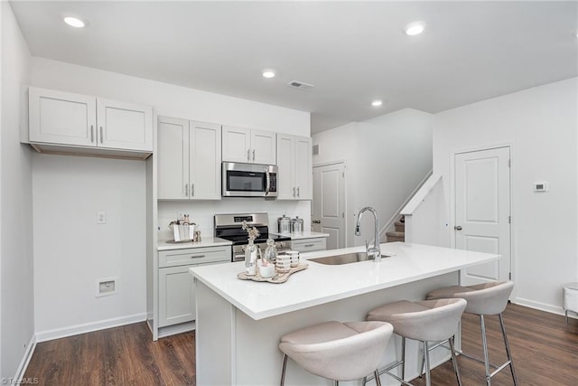 kitchen with dark hardwood / wood-style floors, appliances with stainless steel finishes, sink, and an island with sink