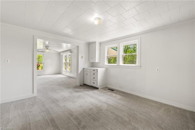 interior space with crown molding, light colored carpet, ceiling fan, visible vents, and baseboards