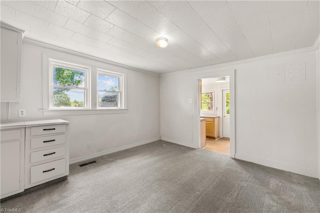 unfurnished bedroom featuring connected bathroom, crown molding, visible vents, baseboards, and light carpet