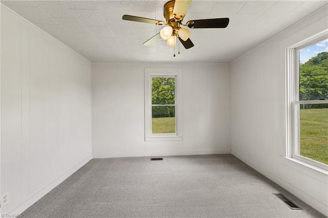carpeted spare room featuring visible vents, a ceiling fan, and a healthy amount of sunlight