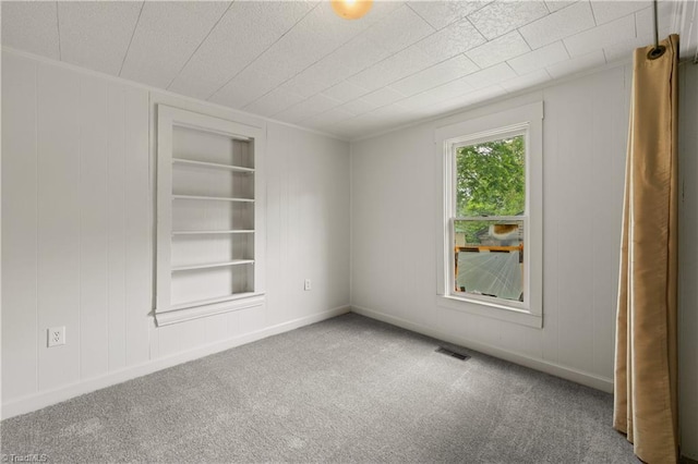 unfurnished room with carpet flooring, visible vents, built in features, and a decorative wall