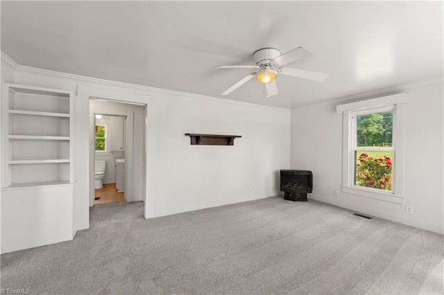 empty room with ornamental molding, a wood stove, a ceiling fan, and carpet floors