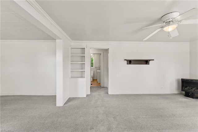 unfurnished living room featuring ceiling fan, built in features, baseboards, ornamental molding, and carpet floors
