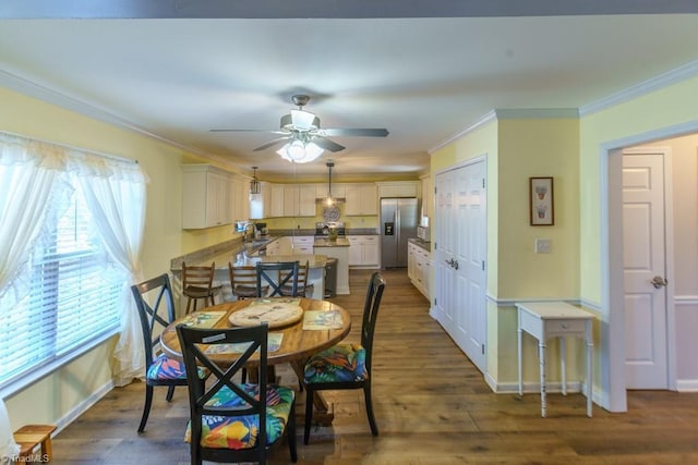 dining space with sink, dark wood-type flooring, ornamental molding, and ceiling fan