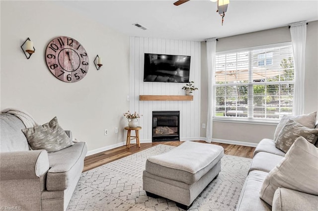 living room with wood finished floors, visible vents, a large fireplace, a ceiling fan, and baseboards