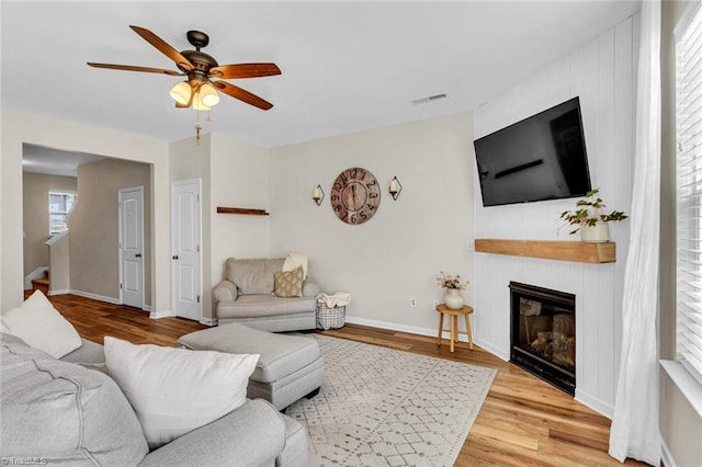 living area with a ceiling fan, baseboards, visible vents, wood finished floors, and a large fireplace
