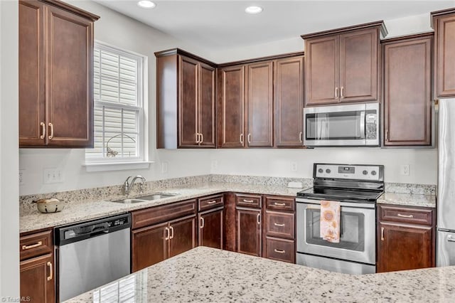 kitchen featuring a wealth of natural light, light stone counters, appliances with stainless steel finishes, and a sink