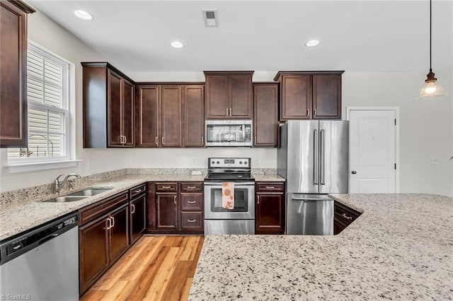kitchen featuring appliances with stainless steel finishes, dark brown cabinets, visible vents, a sink, and light wood-type flooring