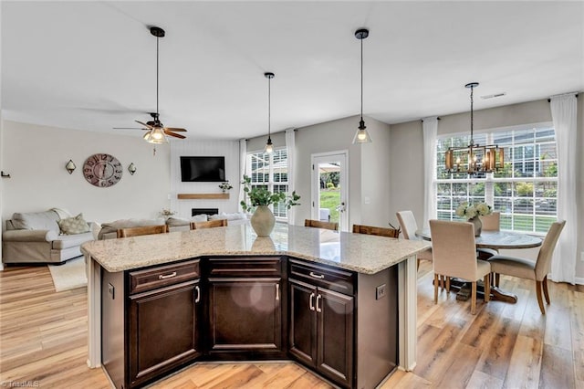 kitchen featuring light wood-style flooring, dark brown cabinets, ceiling fan with notable chandelier, open floor plan, and a fireplace