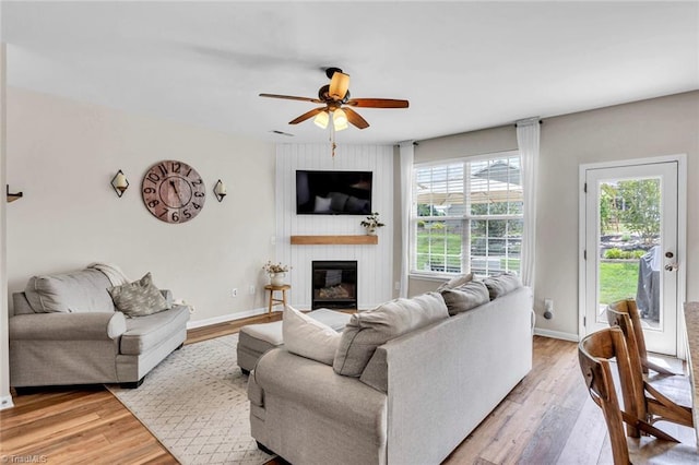 living area featuring a large fireplace, baseboards, ceiling fan, and light wood finished floors