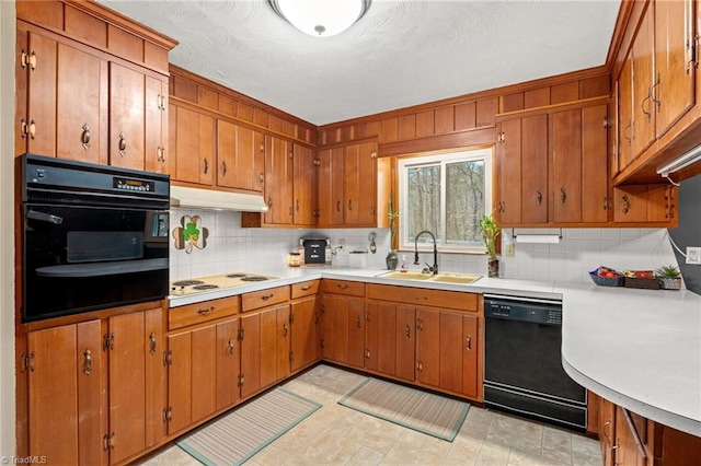 kitchen featuring a sink, black appliances, light countertops, under cabinet range hood, and brown cabinets