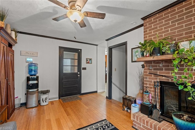 entryway featuring a ceiling fan, a fireplace, light wood-style flooring, and crown molding