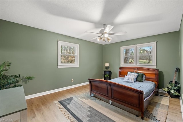 bedroom featuring ceiling fan, baseboards, a textured ceiling, and light wood-style flooring