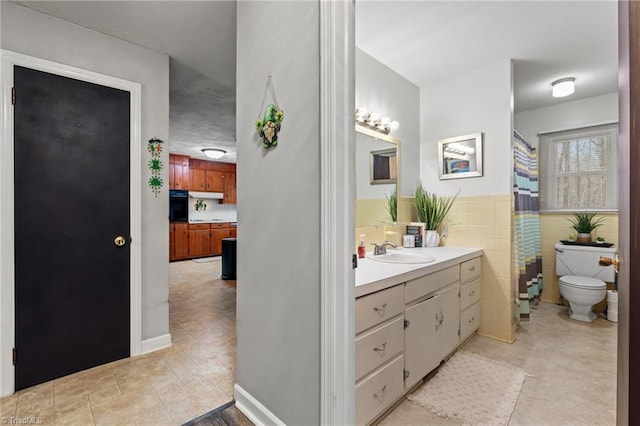 bathroom featuring vanity, a wainscoted wall, tile patterned flooring, tile walls, and toilet