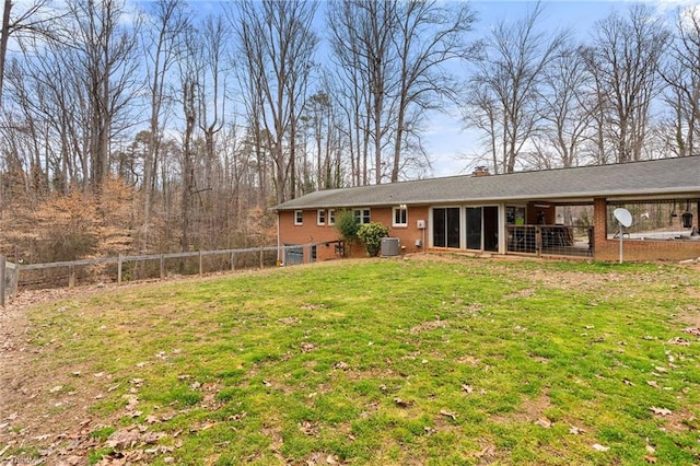 back of property with cooling unit, a yard, a fenced backyard, a chimney, and brick siding