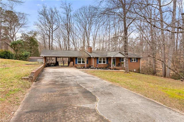 ranch-style house featuring brick siding, an attached carport, concrete driveway, a front yard, and a chimney