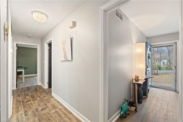 hall featuring visible vents, baseboards, and wood finished floors