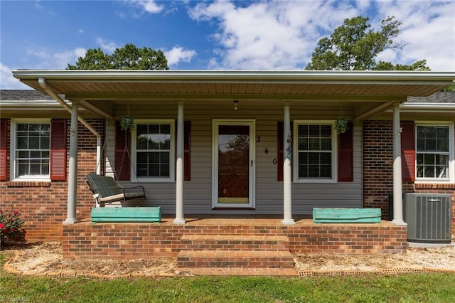 view of exterior entry with a porch, central AC, and brick siding