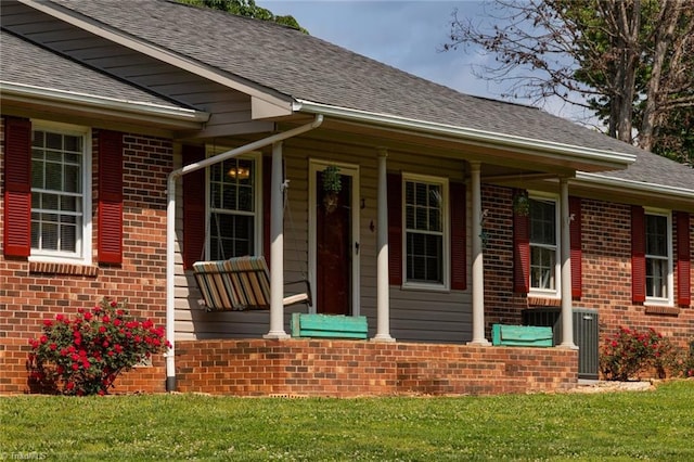 doorway to property featuring brick siding, a shingled roof, a yard, and a porch
