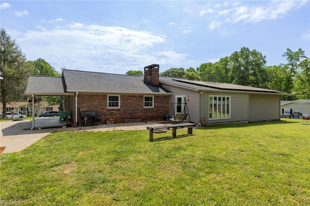 rear view of property featuring an attached carport, roof mounted solar panels, a chimney, a yard, and driveway