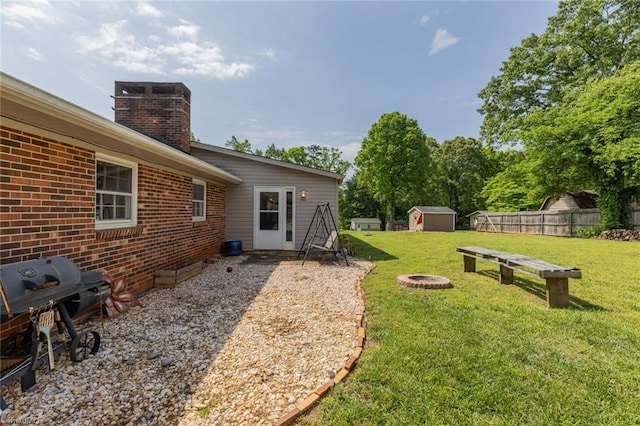 view of yard with fence, an outdoor structure, an outdoor fire pit, and a shed