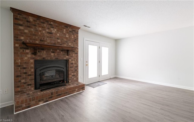 909 Shelby Dr Unit B, Greensboro, NC 27409 - unfurnished living room with wood finished floors, baseboards, a brick fireplace, and a textured ceiling