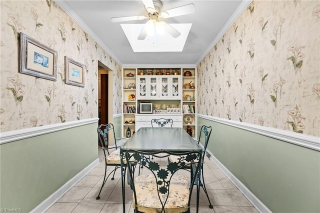 tiled dining space with ceiling fan, a skylight, built in features, and crown molding