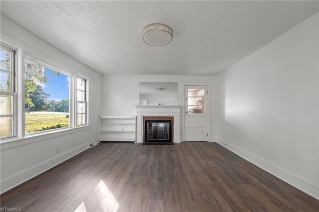 unfurnished living room featuring a textured ceiling, dark hardwood / wood-style flooring, a wealth of natural light, and a fireplace