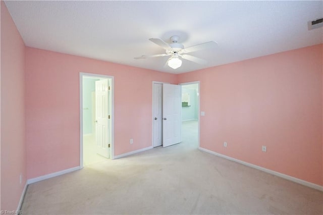 unfurnished bedroom featuring ceiling fan, light colored carpet, ensuite bathroom, and a closet