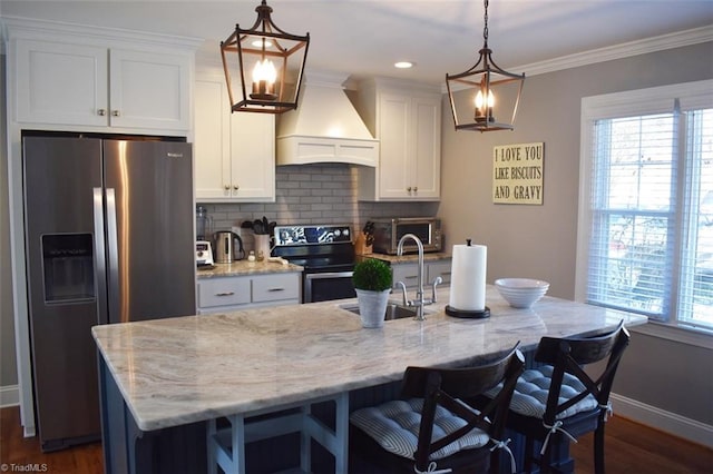 kitchen featuring decorative light fixtures, appliances with stainless steel finishes, an island with sink, and custom range hood