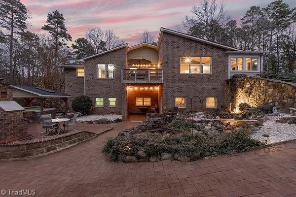 back house at dusk with a balcony, exterior kitchen, and a patio