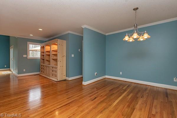 spare room featuring an inviting chandelier, wood-type flooring, and ornamental molding