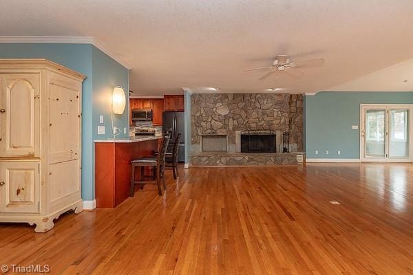 living room with crown molding, ceiling fan, a stone fireplace, and hardwood / wood-style floors