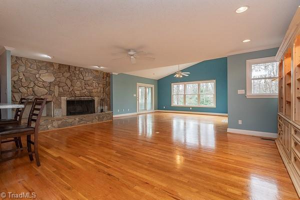 unfurnished living room with ceiling fan, a stone fireplace, vaulted ceiling, and light hardwood / wood-style flooring