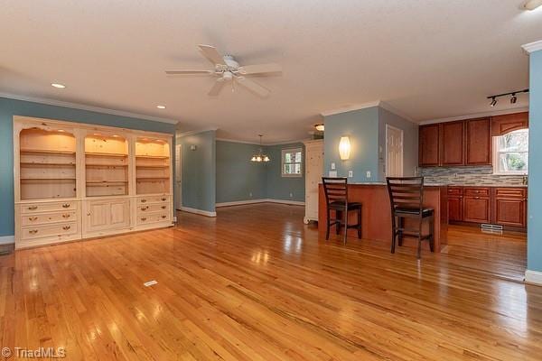 unfurnished living room featuring crown molding, ceiling fan with notable chandelier, and light wood-type flooring