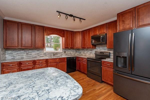 kitchen featuring tasteful backsplash, sink, light hardwood / wood-style floors, and black appliances