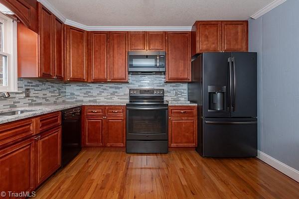 kitchen featuring light hardwood / wood-style flooring, decorative backsplash, light stone counters, and black appliances